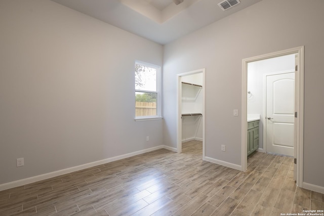 unfurnished bedroom featuring a spacious closet, a closet, ensuite bathroom, and light wood-type flooring