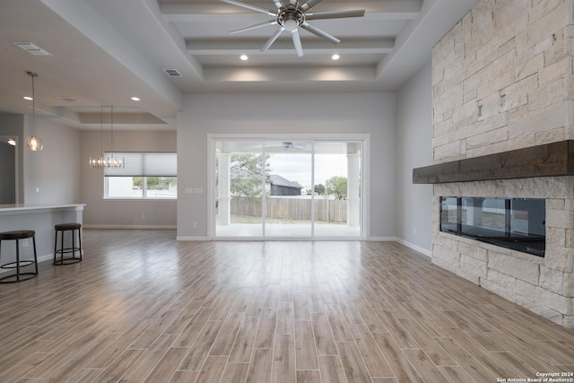 unfurnished living room with ceiling fan with notable chandelier, light hardwood / wood-style floors, a stone fireplace, and a tray ceiling