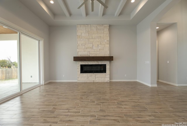 unfurnished living room featuring hardwood / wood-style floors, ceiling fan, a stone fireplace, and beamed ceiling