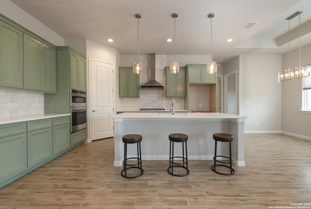 kitchen with green cabinets, light hardwood / wood-style flooring, wall chimney exhaust hood, and decorative light fixtures