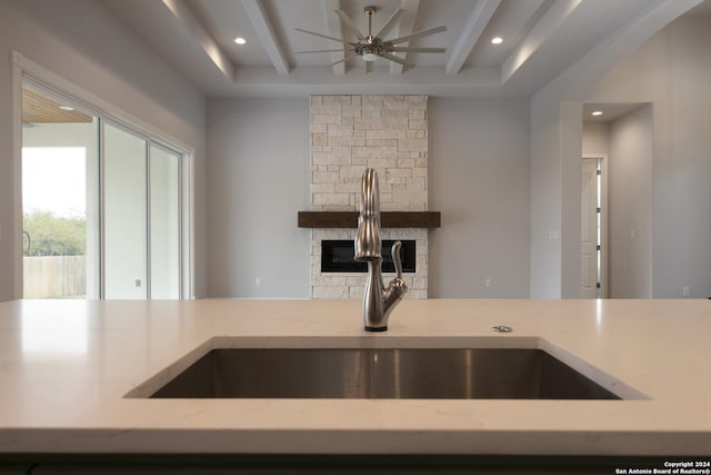 kitchen featuring a fireplace, ceiling fan, a raised ceiling, and sink