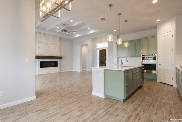 kitchen featuring a kitchen island with sink, green cabinets, sink, light wood-type flooring, and decorative light fixtures