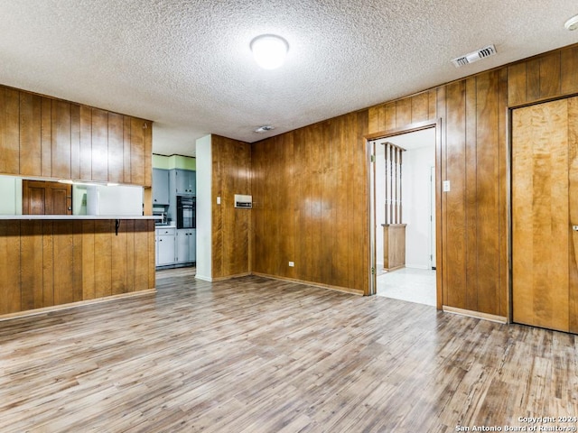 kitchen with wood walls, light hardwood / wood-style floors, and a textured ceiling