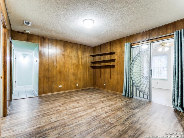 spare room with a textured ceiling, light hardwood / wood-style flooring, and wood walls