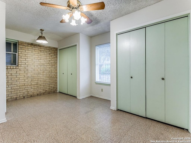 unfurnished bedroom featuring ceiling fan, a textured ceiling, brick wall, and multiple closets