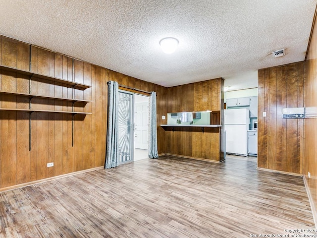 kitchen featuring wood walls, white fridge, light hardwood / wood-style floors, and a textured ceiling