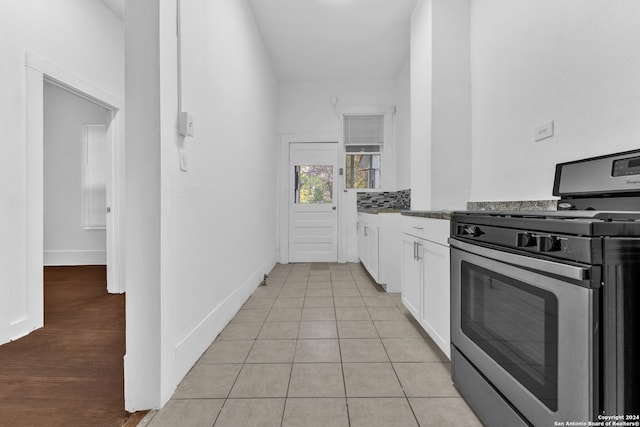 kitchen with stainless steel gas stove, dark stone countertops, white cabinetry, and light tile patterned floors