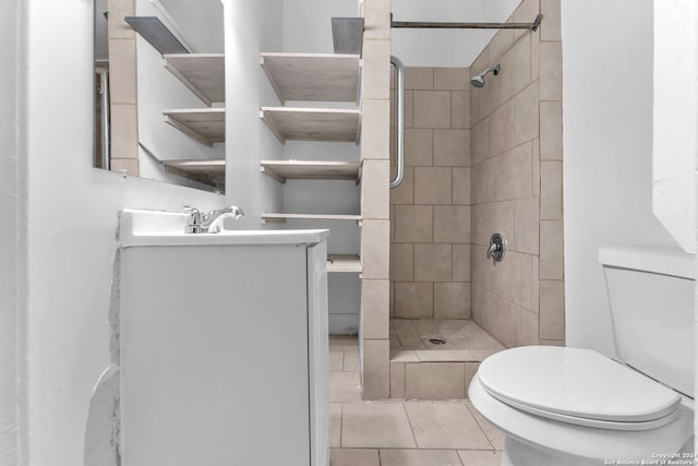 bathroom with tile patterned flooring, vanity, toilet, and a tile shower