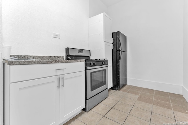 kitchen with white cabinets, black fridge, light tile patterned floors, and stainless steel gas range