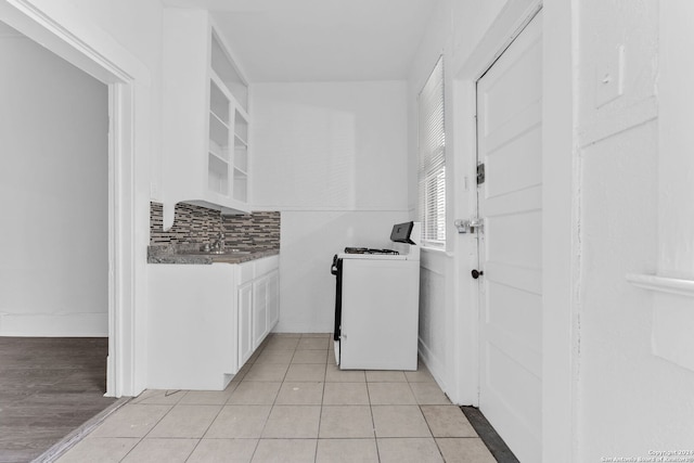 kitchen with white stove, sink, light tile patterned floors, tasteful backsplash, and white cabinetry