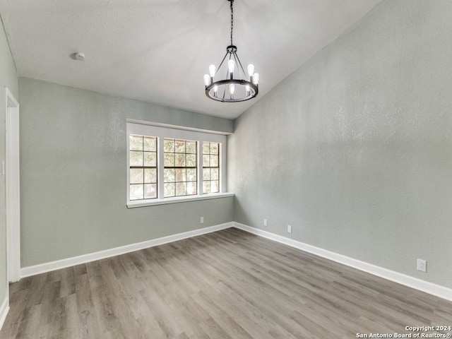 spare room featuring hardwood / wood-style flooring, vaulted ceiling, and an inviting chandelier