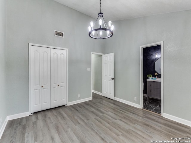 unfurnished bedroom featuring a closet, a towering ceiling, light hardwood / wood-style floors, and a notable chandelier