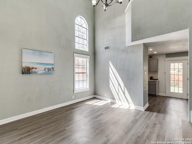 unfurnished living room with a towering ceiling, a chandelier, and hardwood / wood-style flooring