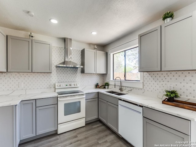 kitchen with gray cabinetry, sink, wall chimney exhaust hood, white appliances, and light wood-type flooring