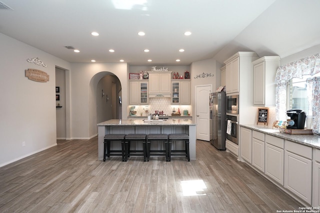 kitchen featuring light stone counters, a spacious island, a breakfast bar area, appliances with stainless steel finishes, and light wood-type flooring