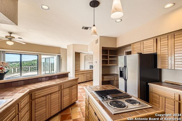 kitchen with tile countertops, stainless steel refrigerator with ice dispenser, white electric stovetop, hanging light fixtures, and ceiling fan