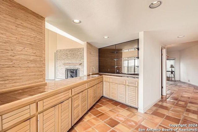 kitchen featuring a fireplace, light tile patterned floors, tile counters, and sink