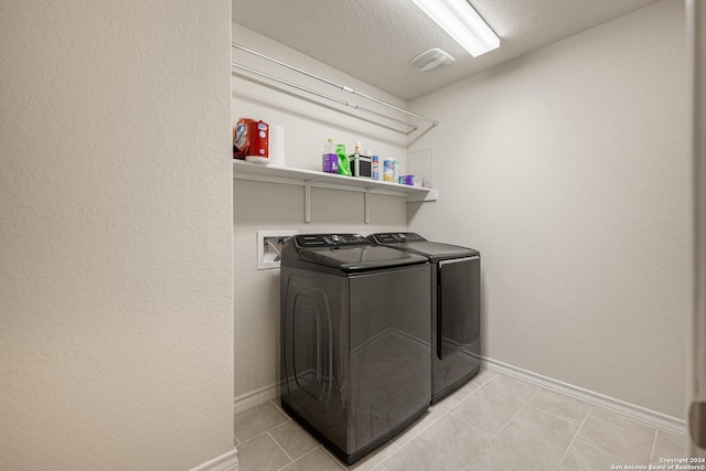 clothes washing area featuring a textured ceiling, separate washer and dryer, and light tile patterned flooring