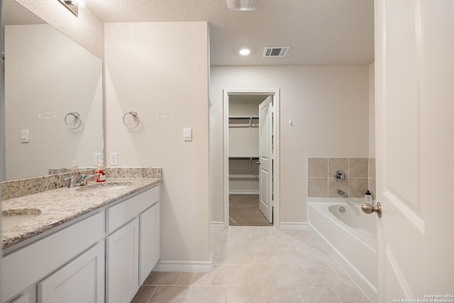 bathroom with tile patterned flooring, vanity, a textured ceiling, and a tub