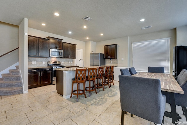 kitchen featuring appliances with stainless steel finishes, tasteful backsplash, dark brown cabinetry, a breakfast bar area, and an island with sink