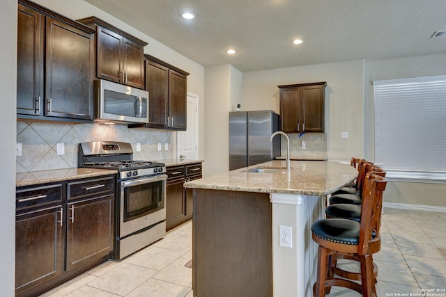 kitchen with sink, an island with sink, light tile patterned floors, and appliances with stainless steel finishes