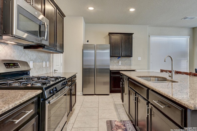 kitchen with appliances with stainless steel finishes, backsplash, light stone counters, sink, and light tile patterned floors