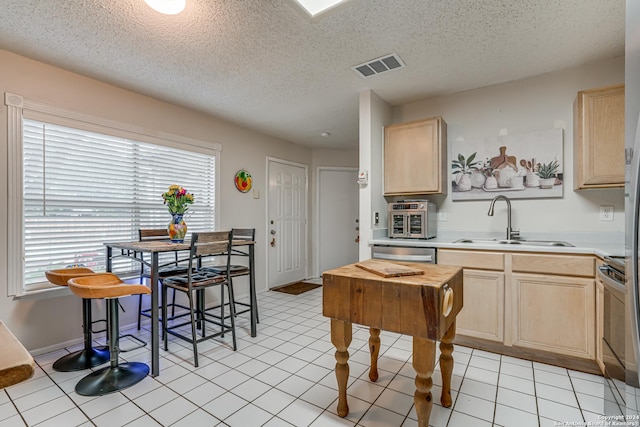 kitchen featuring light brown cabinetry, stainless steel dishwasher, a textured ceiling, sink, and light tile patterned flooring