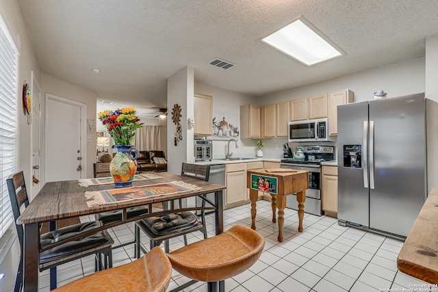 kitchen with light brown cabinetry, a textured ceiling, stainless steel appliances, and sink