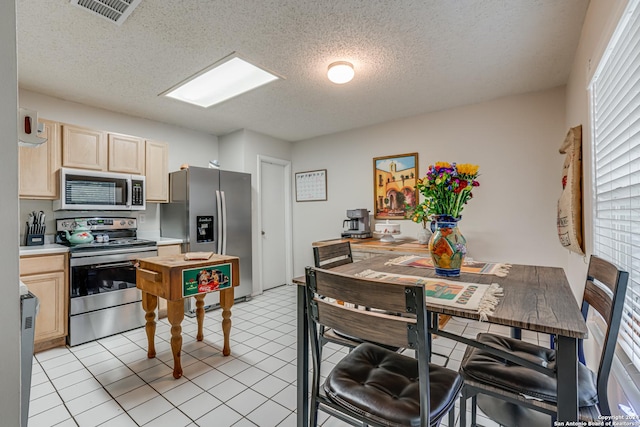 kitchen with a textured ceiling, light tile patterned floors, stainless steel appliances, and light brown cabinetry