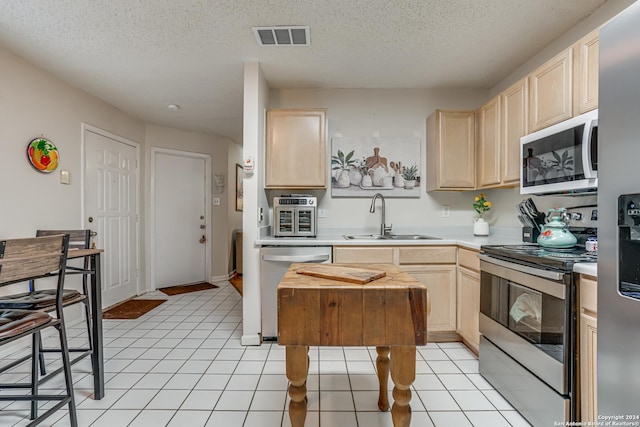 kitchen featuring light brown cabinets, a textured ceiling, stainless steel appliances, and sink