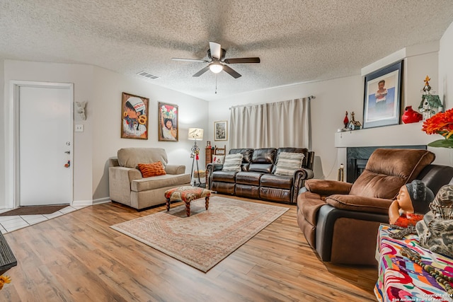 living room featuring ceiling fan, a textured ceiling, and light wood-type flooring