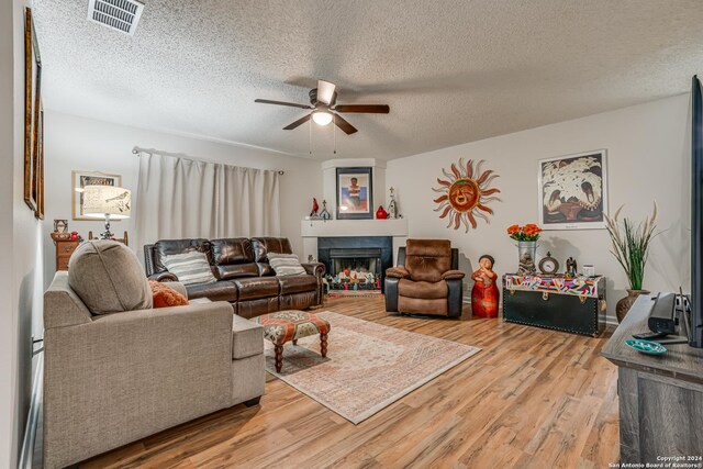 living room featuring ceiling fan, a textured ceiling, and light hardwood / wood-style flooring