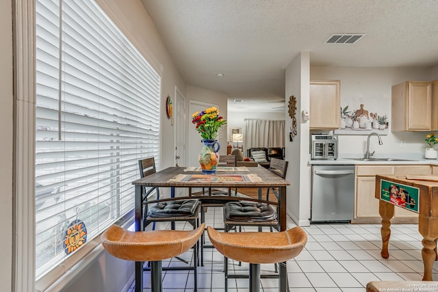 kitchen with light brown cabinets, a textured ceiling, stainless steel dishwasher, and sink