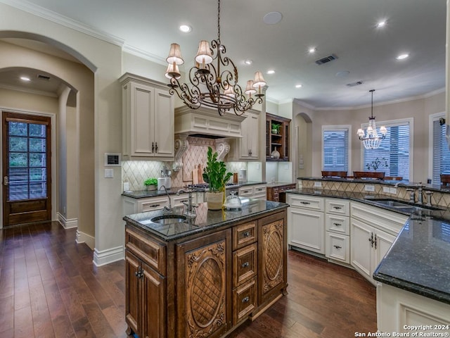 kitchen with a center island with sink, sink, hanging light fixtures, and dark wood-type flooring