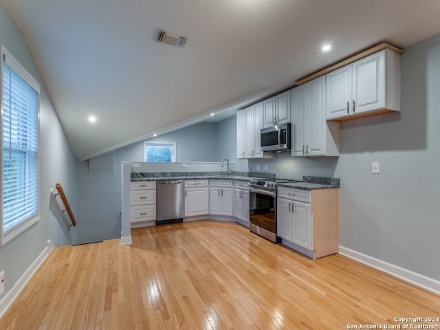 kitchen with lofted ceiling, white cabinets, sink, light wood-type flooring, and stainless steel appliances