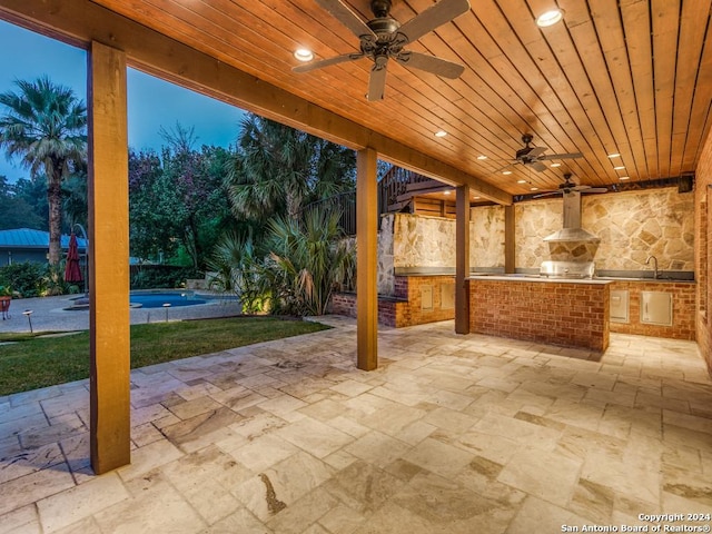 patio terrace at dusk featuring a lawn, ceiling fan, and exterior kitchen