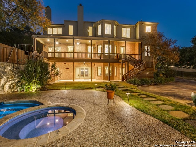 back house at night with a patio area, an in ground hot tub, and french doors