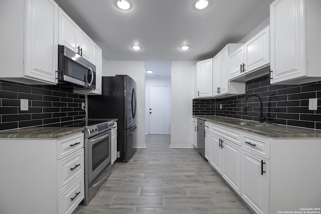 kitchen featuring backsplash, dark stone counters, white cabinets, sink, and appliances with stainless steel finishes