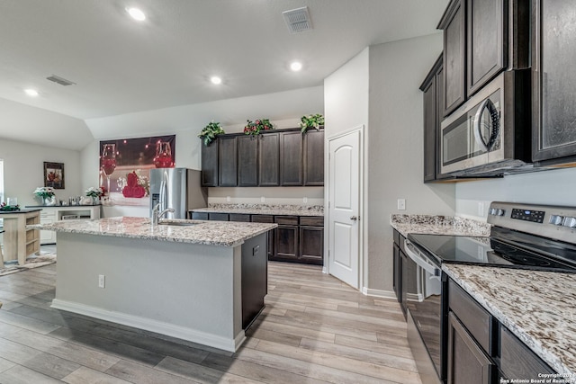 kitchen with light stone countertops, appliances with stainless steel finishes, light wood-type flooring, sink, and a center island with sink