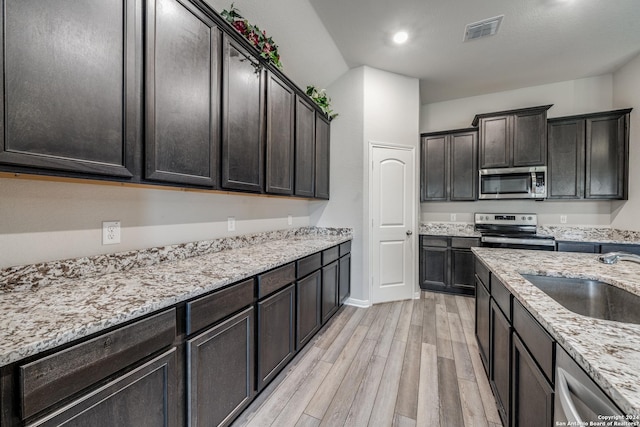 kitchen featuring light stone counters, dark brown cabinetry, stainless steel appliances, sink, and light hardwood / wood-style floors