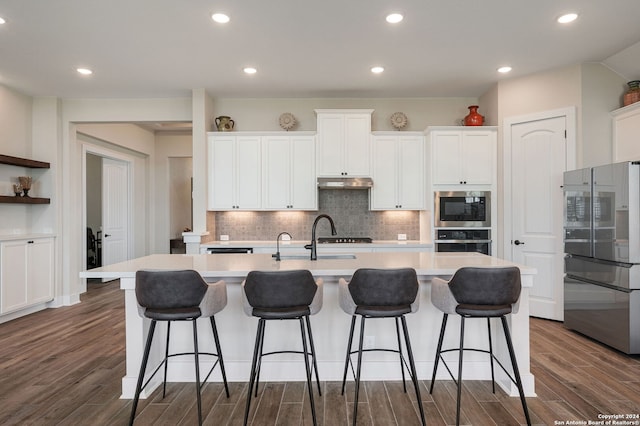 kitchen with white cabinets, dark hardwood / wood-style floors, an island with sink, and stainless steel appliances