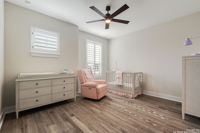 bedroom featuring a nursery area, ceiling fan, and wood-type flooring