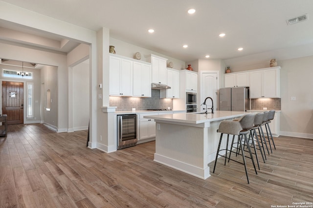 kitchen featuring white cabinetry, light hardwood / wood-style flooring, beverage cooler, and a center island with sink