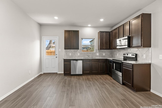 kitchen with appliances with stainless steel finishes, light stone counters, dark brown cabinets, and hardwood / wood-style floors