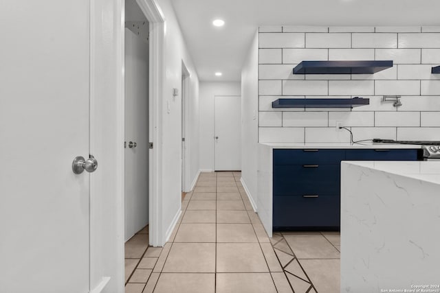 kitchen featuring blue cabinetry, decorative backsplash, light stone counters, and light tile patterned floors