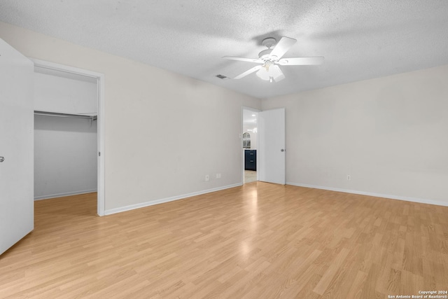 unfurnished bedroom with ceiling fan, a spacious closet, a textured ceiling, light hardwood / wood-style floors, and a closet