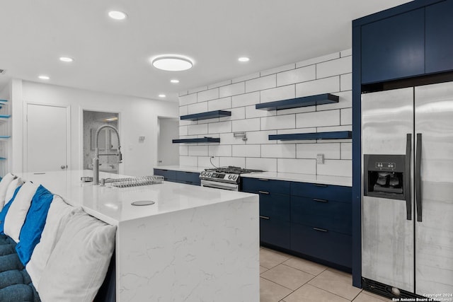 kitchen featuring tasteful backsplash, stainless steel appliances, blue cabinetry, light tile patterned floors, and an island with sink