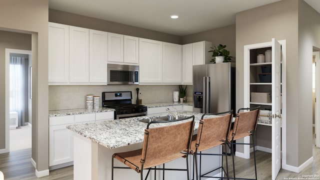 kitchen with a kitchen bar, appliances with stainless steel finishes, light stone counters, white cabinetry, and an island with sink