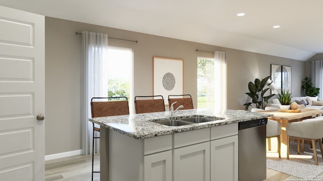 kitchen with a center island with sink, sink, light hardwood / wood-style flooring, stainless steel dishwasher, and light stone counters