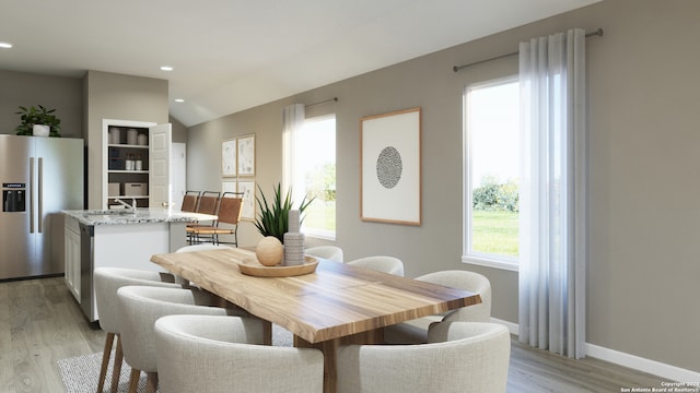 dining space with sink, vaulted ceiling, and light wood-type flooring